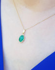 Gold necklace with an emerald pendant on a person wearing a blue and white outfit.