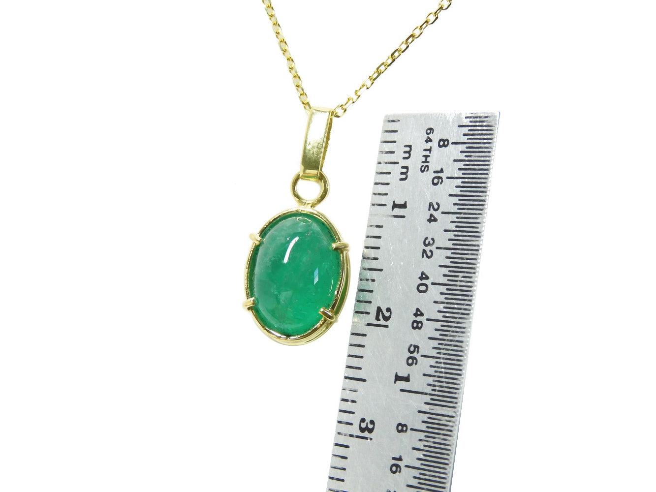 A 18k gold emerald cabochon pendant next to a ruler for scale on a white background.