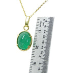A 18k gold emerald cabochon pendant next to a ruler for scale on a white background.