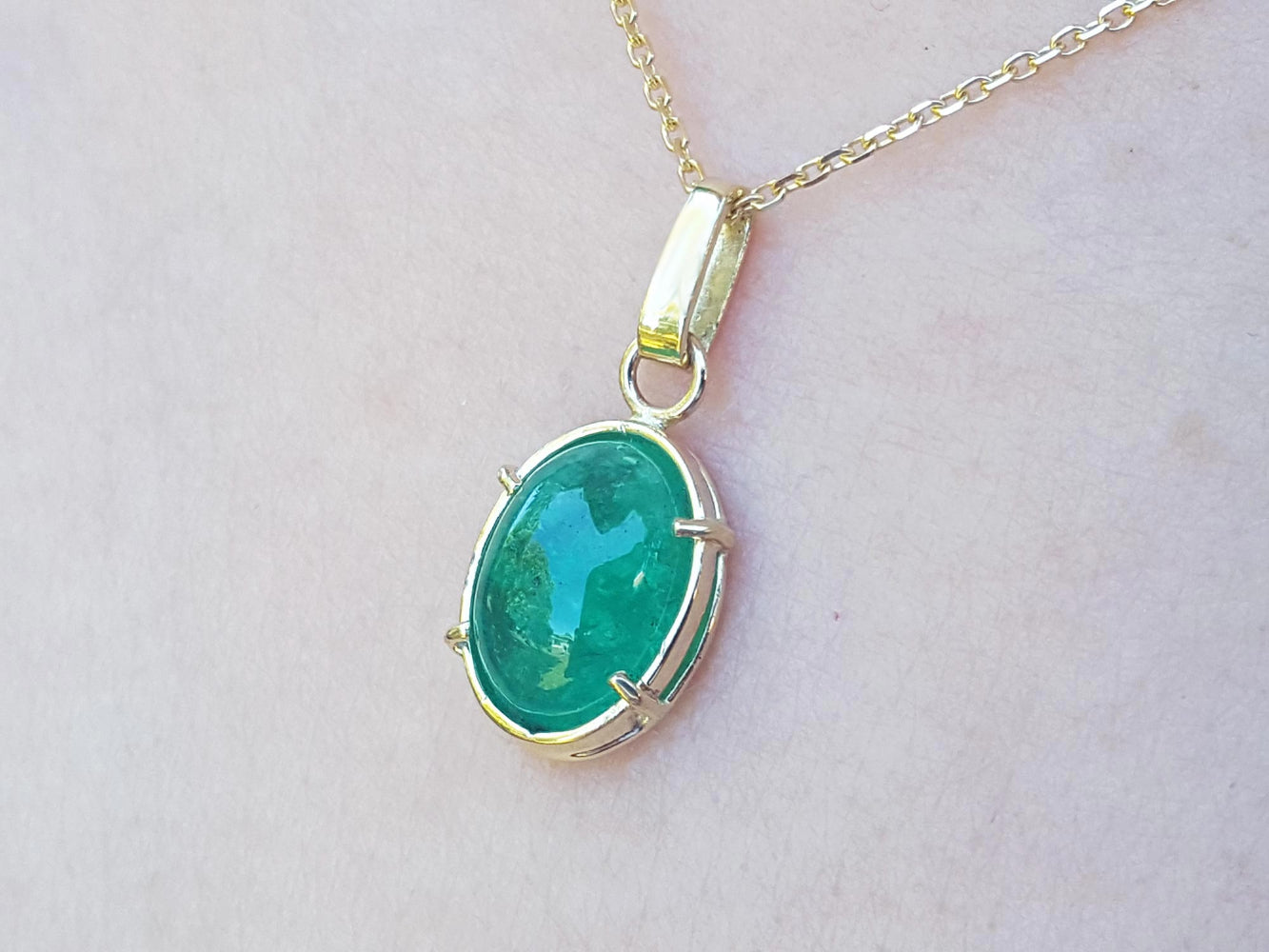 A cabochon emerald pendant on a gold chain against a light background