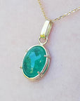 A cabochon emerald pendant on a gold chain against a light background
