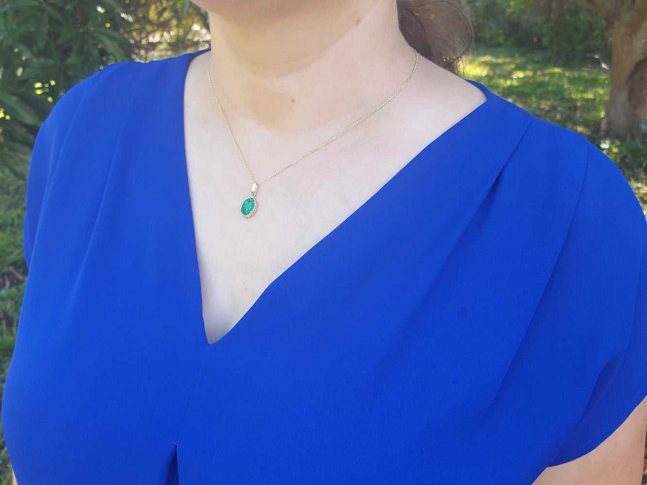 A woman wearing a blue top with a necklace Colombian emerald cabochon pendant.