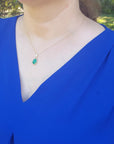 A woman wearing a blue top with a necklace Colombian emerald cabochon pendant.