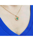 14k yellow gold necklace with an oval Colombian emerald and diamond pendant on a blue top.