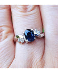 14k white gold ring with a blue oval cut sapphire on a person's finger.