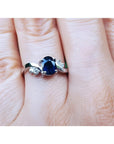 1.43 ct oval natural deep blue sapphire ring with accent diamonds set in 14K white gold on a hand.
