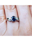 1.43 ct oval natural deep blue sapphire ring with accent diamonds set in 14K white gold on a hand.