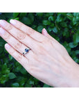 Hand wearing a white gold ring with a blue sapphire against a green leafy background