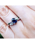 14k gold ring with a blue sapphire gemstone on a finger against a white background