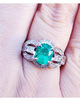 A 18k white gold oval cut colombian emerald ring with accent diamonds on a finger