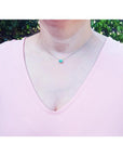 Emerald necklace with oval cut halo diamonds in 14K white gold, worn on a woman.