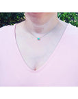 Emerald necklace with oval cut halo diamonds in 14K white gold, worn on a woman.