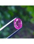 Sparkling 2.38 carat oval cut natural Mozambique ruby, held by tweezers against a green background.
