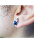 Oval blue sapphire stud earring with three small diamonds in 14K white gold on an ear.