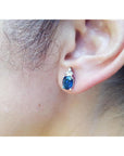 Close-up of an ear wearing a blue oval cut sapphire gemstone earring.