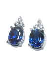 Oval deep blue sapphire stud earrings with three prong-set diamonds in 14K white gold.