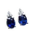 Oval deep blue sapphire stud earrings with three prong-set diamonds in 14K white gold.