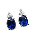 Oval deep blue sapphire stud earrings with three prong-set diamonds in 14K white gold.