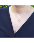 Oval pink sapphire halo diamond pendant necklace in 14K yellow gold on a model.
