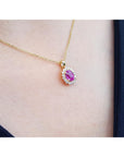 Gold necklace with a pink oval sapphire pendant on a person's neck against a dark background