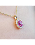 Gold necklace with a pink sapphire gemstone pendant on a person's neck.