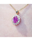 Pink oval cut sapphire gemstone halo diamond pendant with gold chain on a light skin background