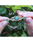 Gold bracelet with real colombian emeralds held between fingers against a leafy background.