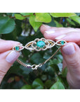 Gold bracelet with real colombian emeralds held between fingers against a leafy background.