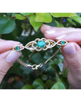 Vintage 14K yellow gold bracelet with oval emeralds and diamonds, held against green leaves.
