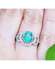 Clover ring with an oval cut emerald on a person's finger against a natural background.