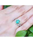 Oval emerald clover ring with diamond halo in 14K white gold on a hand.