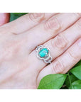 Oval emerald clover ring with diamond halo in 14K white gold on a hand.