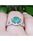 14K white gold clover ring with a 1.55 ct oval emerald center and diamond halo.
