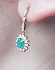 Close-up of a gold earring with an oval cut emerald yellow gold on a person's ear.