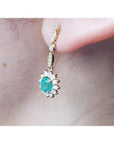 Oval emerald and halo diamond dangle earrings in 14K yellow gold, worn on an ear.
