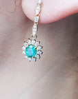 Close-up of an oval cut emerald encircled by a halo diamond earring on an ear.