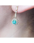 14K yellow gold dangle earring with oval emerald surrounded by halo diamonds on an ear.