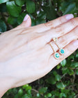Hand displaying a pair of emerald earrings oval cut against a green leafy background