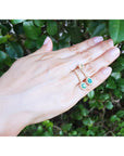 Hand displaying a pair of emerald earrings oval cut against a green leafy background