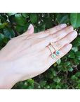 14K yellow gold dangle earrings with oval emeralds and halo diamonds on a hand.