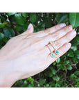 14K yellow gold dangle earrings with oval emeralds and halo diamonds on a hand.