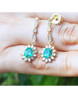 Gold earrings with emerald stones held in a hand against a blurred green background