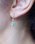 Close-up of an ear wearing a diamond and emerald earring oval cut halo diamond.