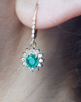 Close-up of a halo diamond oval cut emerald earrings lever backs worn on a woman's ear.