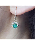 Close-up of a halo diamond oval cut emerald earrings lever backs worn on a woman's ear.