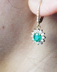 Close-up of a gold earring with a natural emerald oval cut, lever back dangling from an earlobe