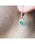 14K gold oval cut emerald earrings with diamond halo and lever backs on an ear.
