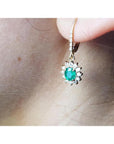 14K gold oval cut emerald earrings with diamond halo and lever backs on an ear.