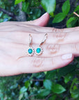 emerald earrings held in a hand with a green leafy background