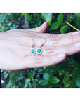 emerald earrings held in a hand with a green leafy background